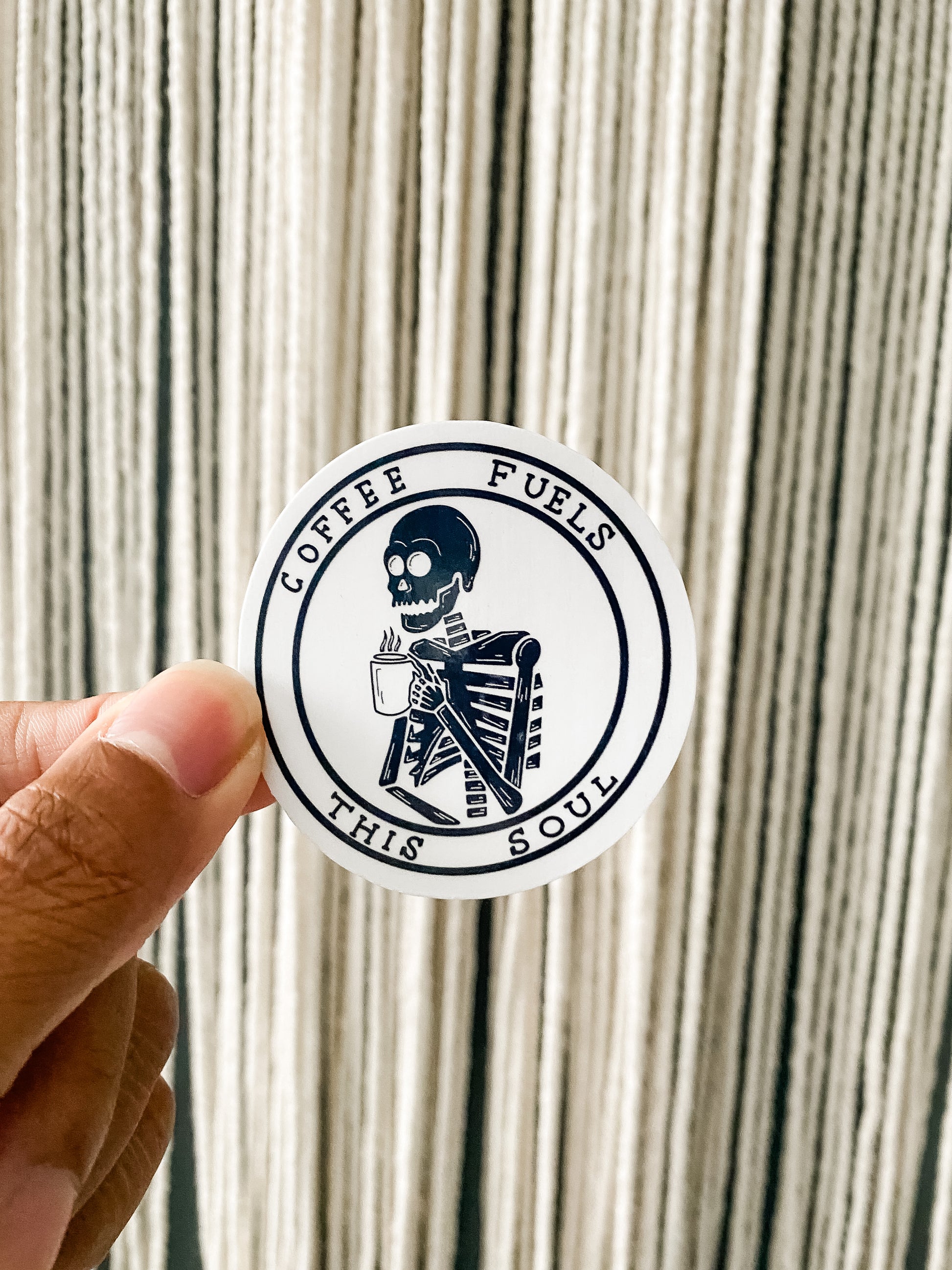 Back and white circle sticker with skeleton holding coffee mug. COFFEE FUELS THIS SOUL around the border